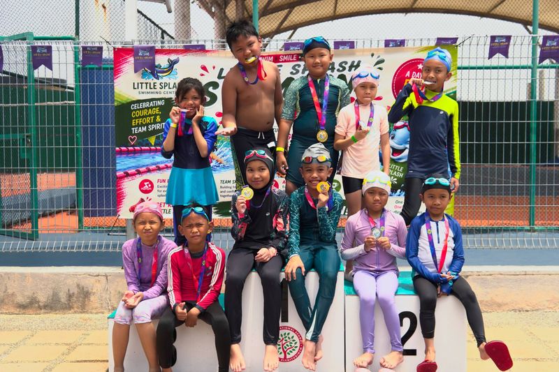 Young swimmers with their medals on the podium in front of the Little Splash Swimming Gala banner